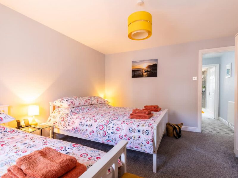 Twin beds in Townhouse Harbour Retreat bedroom with floral bedding and sunset artwork.