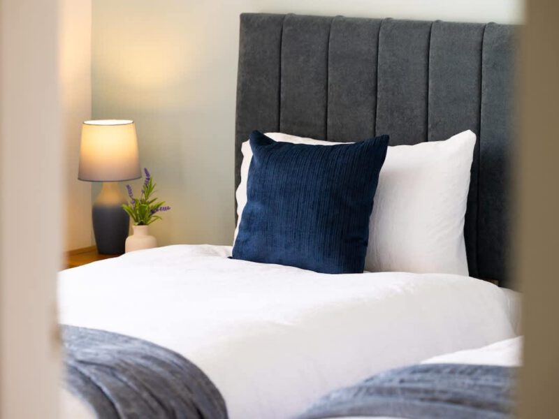 Coastal Village Hideaway: twin beds with navy cushions and bedside lamp.