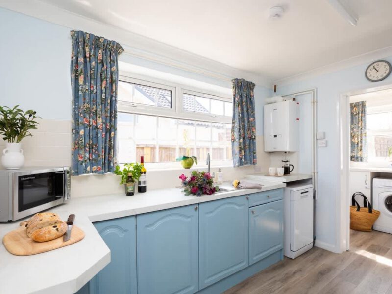 Coastal Village Hideaway kitchen with blue cabinets and floral curtains.