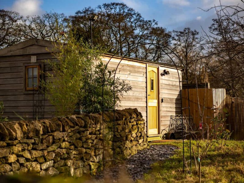 Cosy Shepherd's Hut farm stay with stone wall and garden.