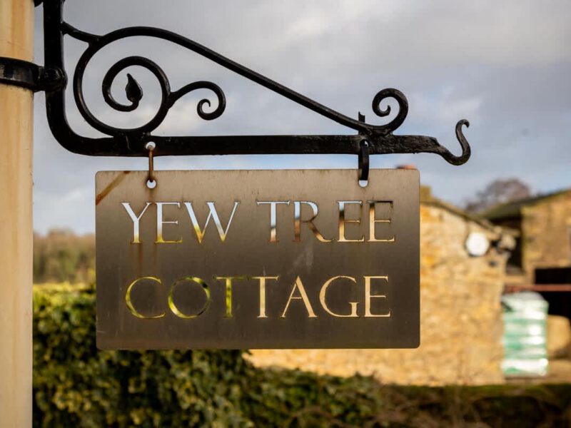 Yew Tree Cottage farm stay sign with rustic stone building background.