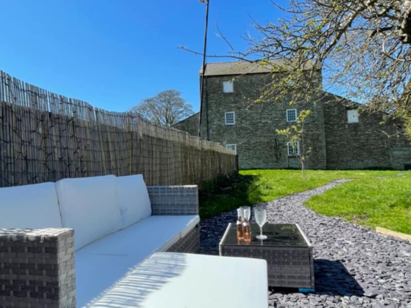 Outdoor seating area with a stone building and garden at Shepherd's Hut farm stay.