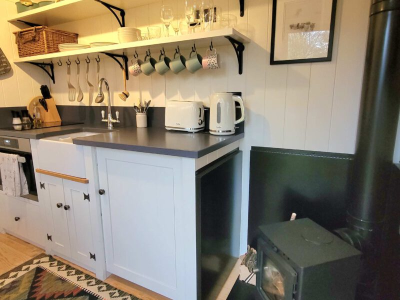 Compact kitchen with wood burner in Plank Bridge shepherds hut.