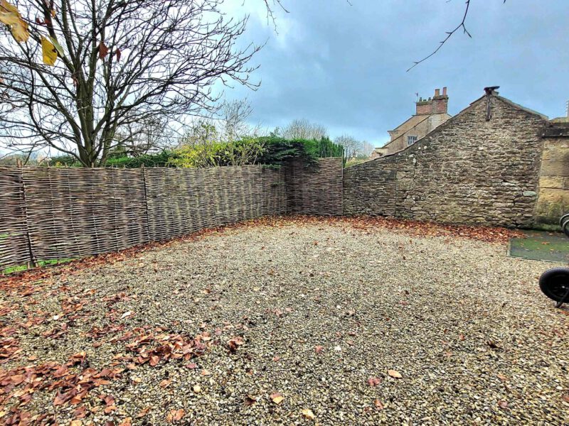 Gravel driveway with stone wall and woven fence at Plank Bridge shepherds hut.