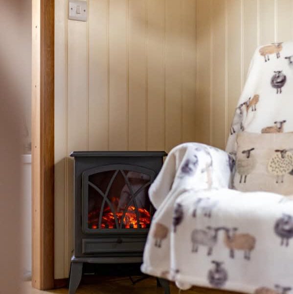 Cosy electric fireplace and sheep-themed chair in Shepherd's Hut farm stay.