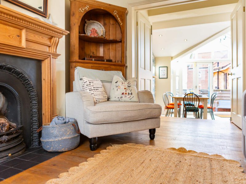 Cozy armchair by fireplace at Harbour View House, with dining area visible.