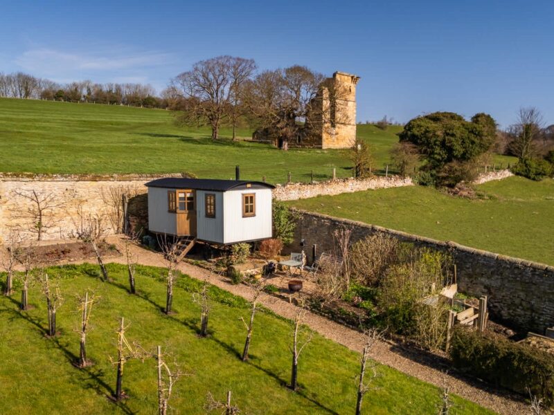 Plank Bridge shepherds hut nestled in an apple orchard with ruins in the background.