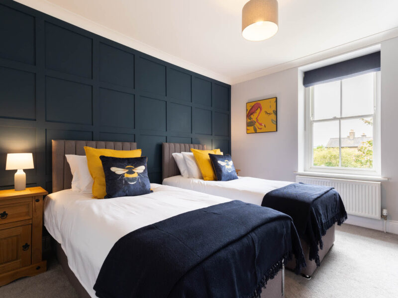 Twin beds with bee-themed decor in Malton Luxury Retreat bedroom.